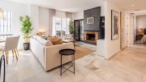 A modern living room with a fireplace, a sofa, a dining area, and a view through a glass door. - Modern penthouse with mountain view - 6 guests (Marbella)