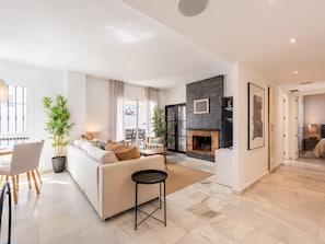 A modern living room with a fireplace, a sofa, a dining area, and a view through a glass door. - Modern penthouse with mountain view - 6 guests (Marbella)