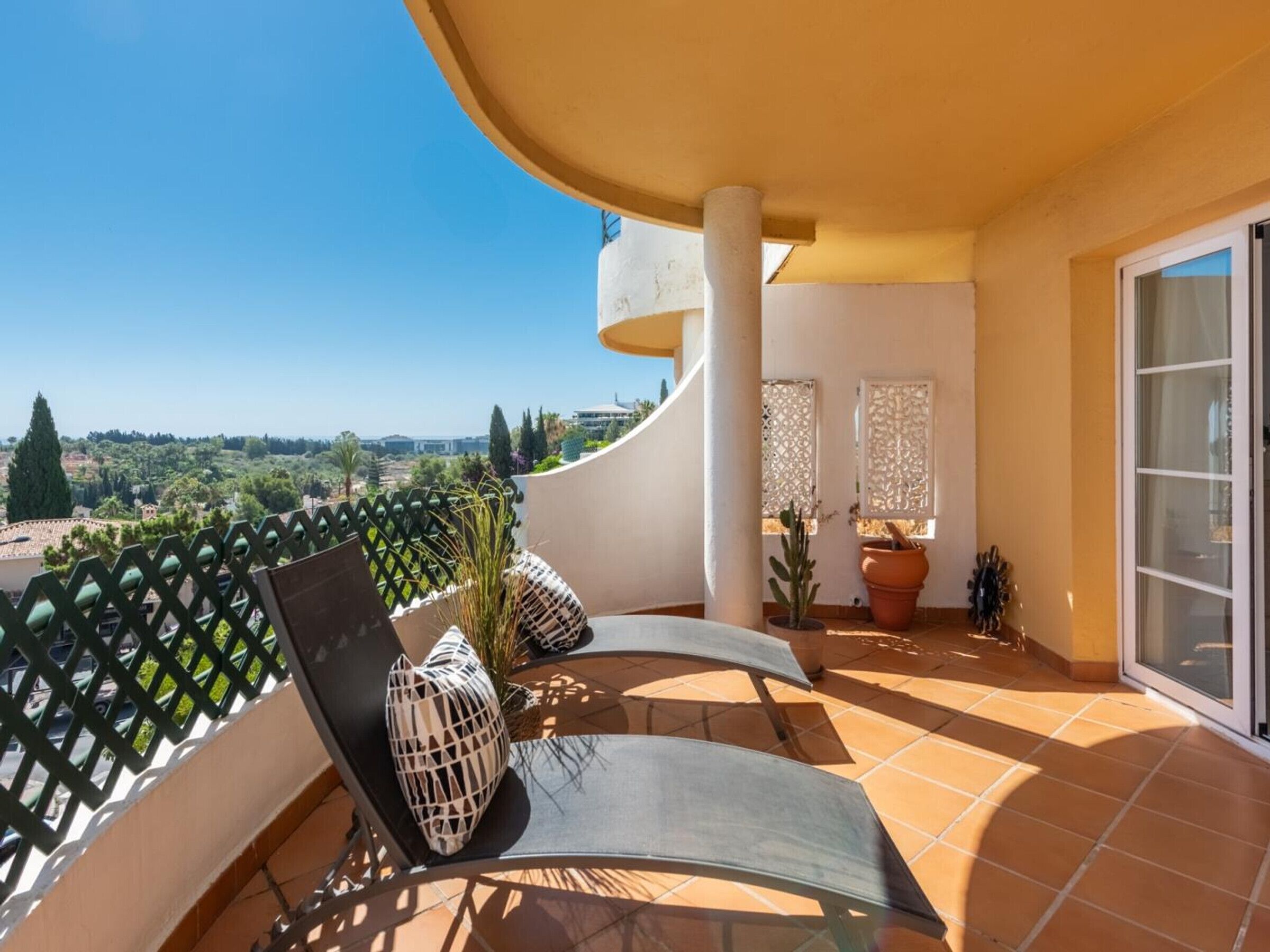 Un balcon doté d’un mur blanc incurvé, d’une porte vitrée et offrant une vue sur le paysage.
