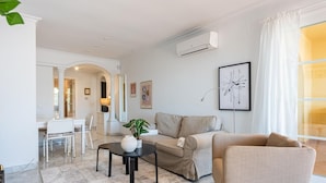 Una sala moderna con un sofá, una silla, una mesa de centro y un comedor con una mesa y sillas.
