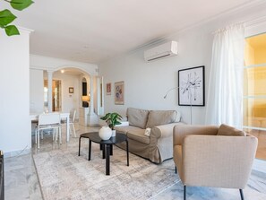 Ein modernes Wohnzimmer mit Sofa, Sessel, Couchtisch und einem Essbereich mit Tisch und Stühlen.