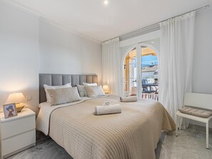 Ein Hotelzimmer mit einem großen Bett, einem Nachttisch mit Lampe, einem Sessel und Blick ins Freie durch eine Glastür.
