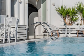 Ein Swimmingpool mit einer Metallleiter, weißen Liegestühlen und einer Palme.