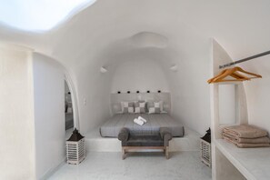 Een kleine slaapkamer met een bed, een bankje, een kledingkast en een hangrek.