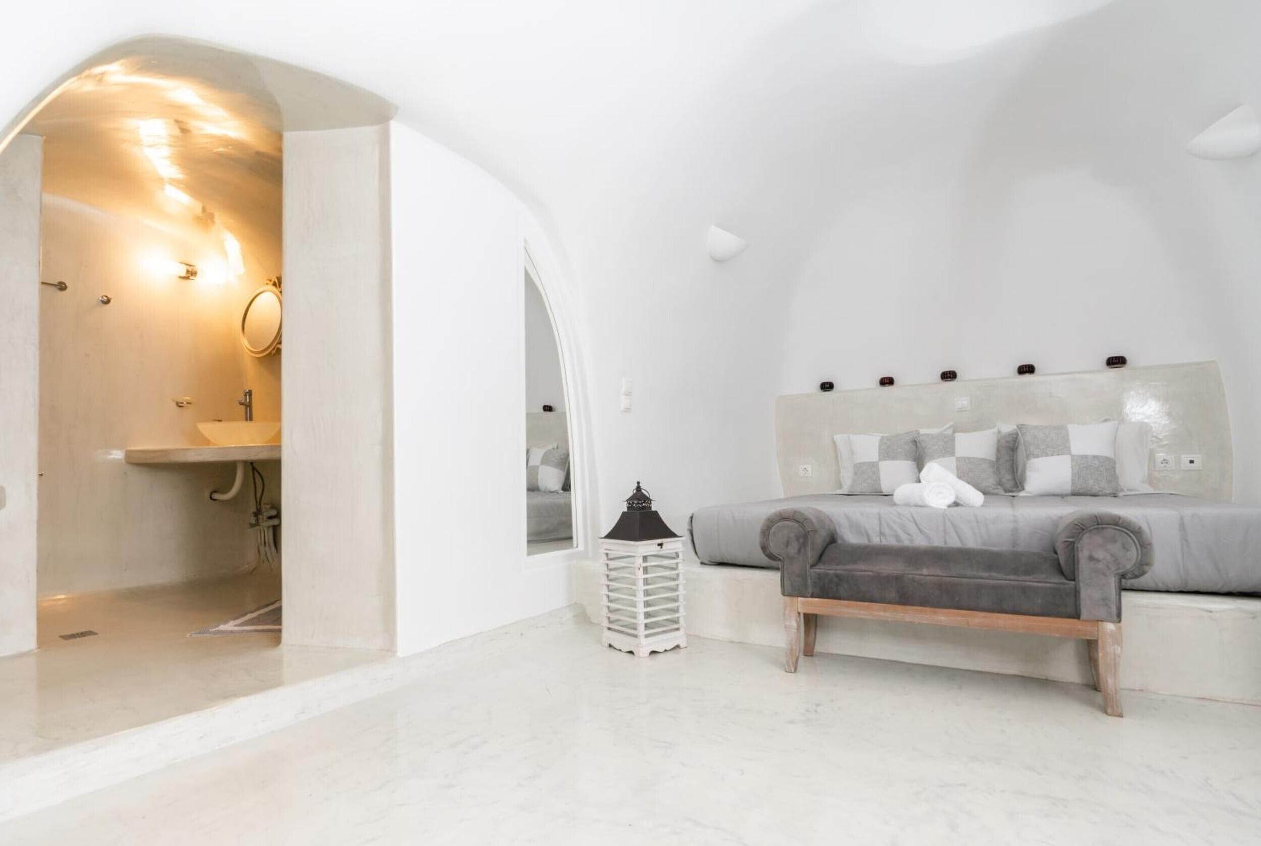 Een moderne slaapkamer met een bed, nachtkastje, lamp en uitzicht op een badkamer.