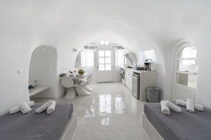 A compact, white interior with a kitchenette, a dining area, and two sleeping areas with rolled towels. - Apartment 'Grand Suite Twin' with Wi-Fi and Air Conditioning (Fira)