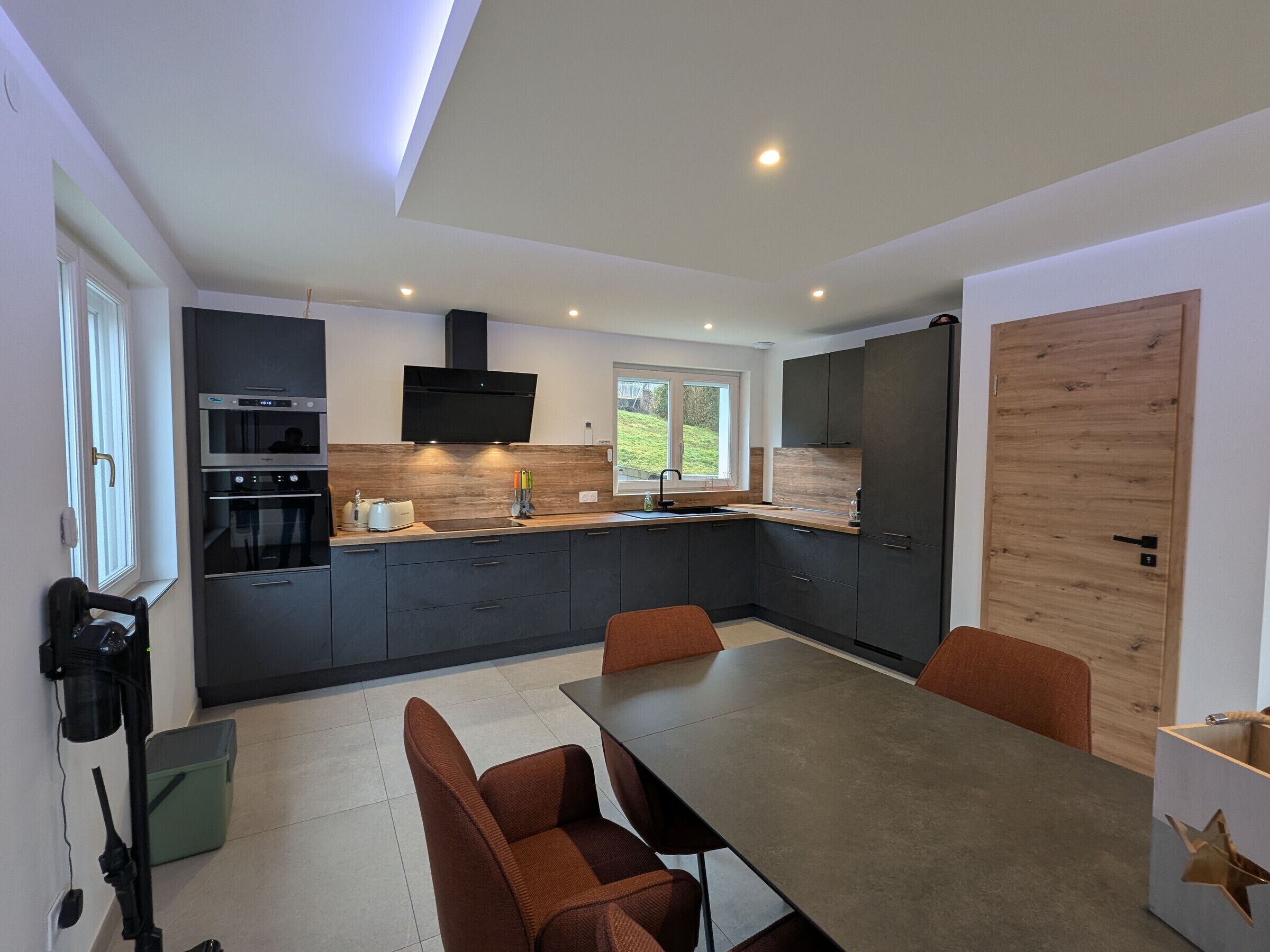 A modern kitchen with dark cabinetry, a built-in oven, a microwave, and a large window.