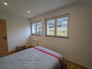 Ein Schlafzimmer mit einem Bett, zwei Fenstern, einer Heizung und einem Holzschrank.