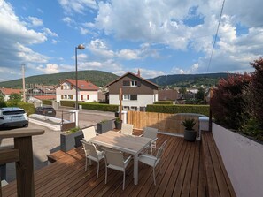 Eine Terrasse mit Tisch und Stühlen, mit Blick auf ein Wohngebiet mit Häusern und einem Berg im Hintergrund.