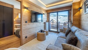 En modern inredning i en timmerstuga med en soffa, en tv och utsikt över bergen.