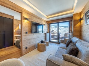 Ein modernes Blockhaus-Interieur mit einer Couch, einem Fernseher und Blick auf die Berge.