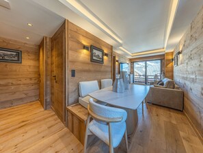 Ein modernes Interieur mit Holzpaneelen, einem Essbereich mit Tisch und Stühlen, einem Sofa und einem an der Wand befestigten Fernseher.