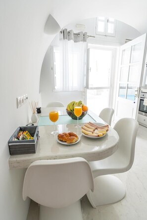 Un comedor blanco con una mesa dispuesta para el desayuno, que incluye croissants, jamón y jugo.
