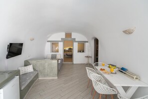 A modern, minimalist living space with a flat-screen TV, a sofa, a dining area with a table and chairs, and a view into the kitchen. - Apartment 'Holiday Home 55sqm' with Wi-Fi and Air Conditioning (Fira)