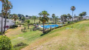 A residential area with a swimming pool, palm trees, and houses in the background. - Modern apartment, panoramic view - 4 guests (Marbella)