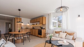 A modern kitchen with wooden cabinets, a dining area with a round table and chairs, a living room with a sofa and a coffee table, and a large window with curtains. - Modern apartment, panoramic view - 4 guests (Marbella)