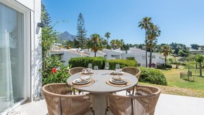 A dining area with a table set for four, surrounded by wicker chairs, overlooking a residential area with houses and greenery. - Modern apartment, panoramic view - 4 guests (Marbella)