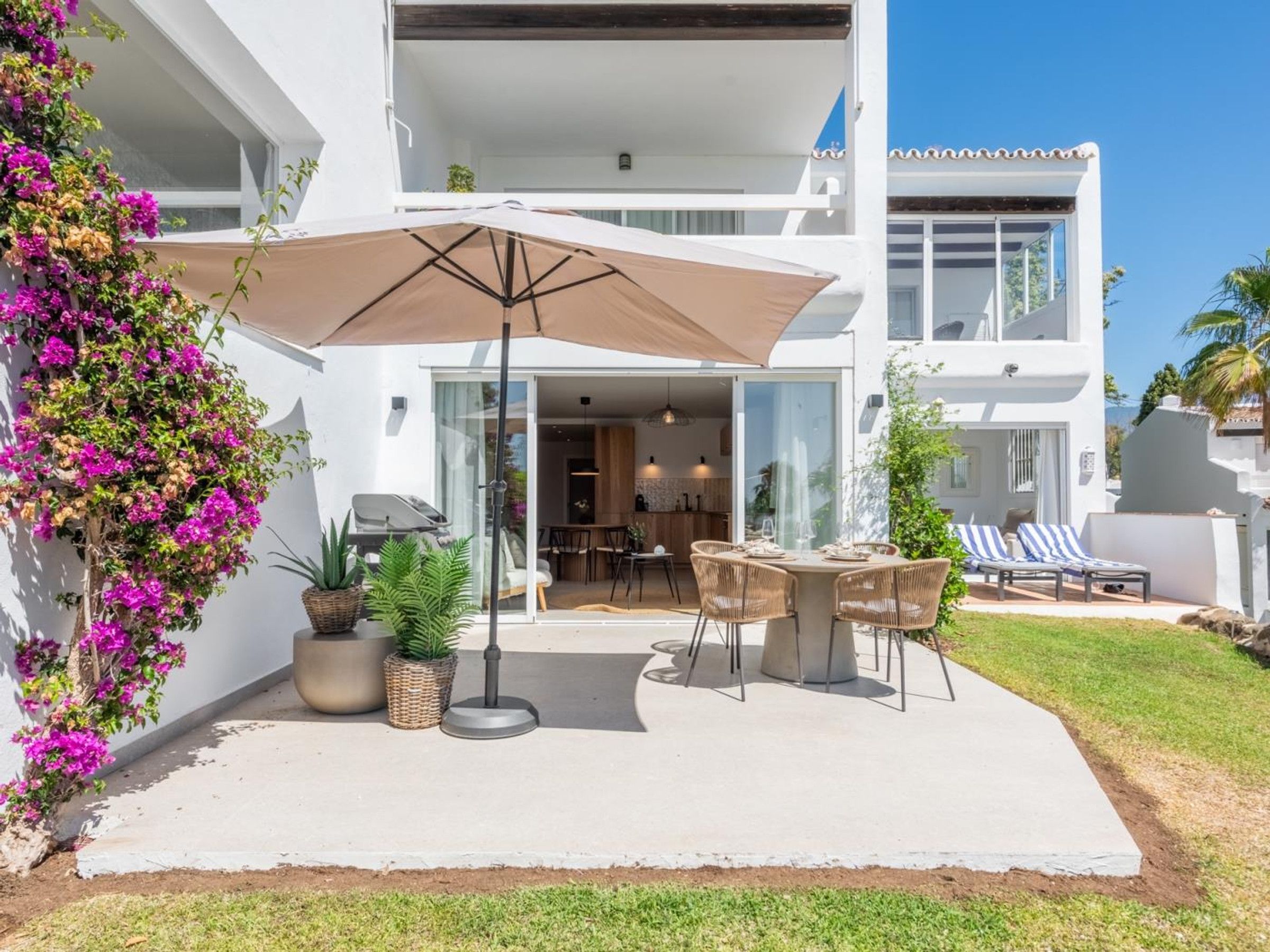 Uma casa moderna de dois andares com um espaço de pátio que inclui uma mesa, cadeiras, churrasqueira e um grande guarda-sol.