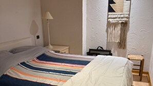 A neatly made bed with a striped bedspread, a bedside lamp, a small table with a bag, and a chair with a woven seat. - Charming lodging in Megève - 6 guests (Megève)