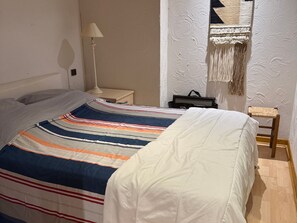 A neatly made bed with a striped bedspread, a bedside lamp, a small table with a bag, and a chair with a woven seat. - Charming lodging in Megève - 6 guests (Megève)