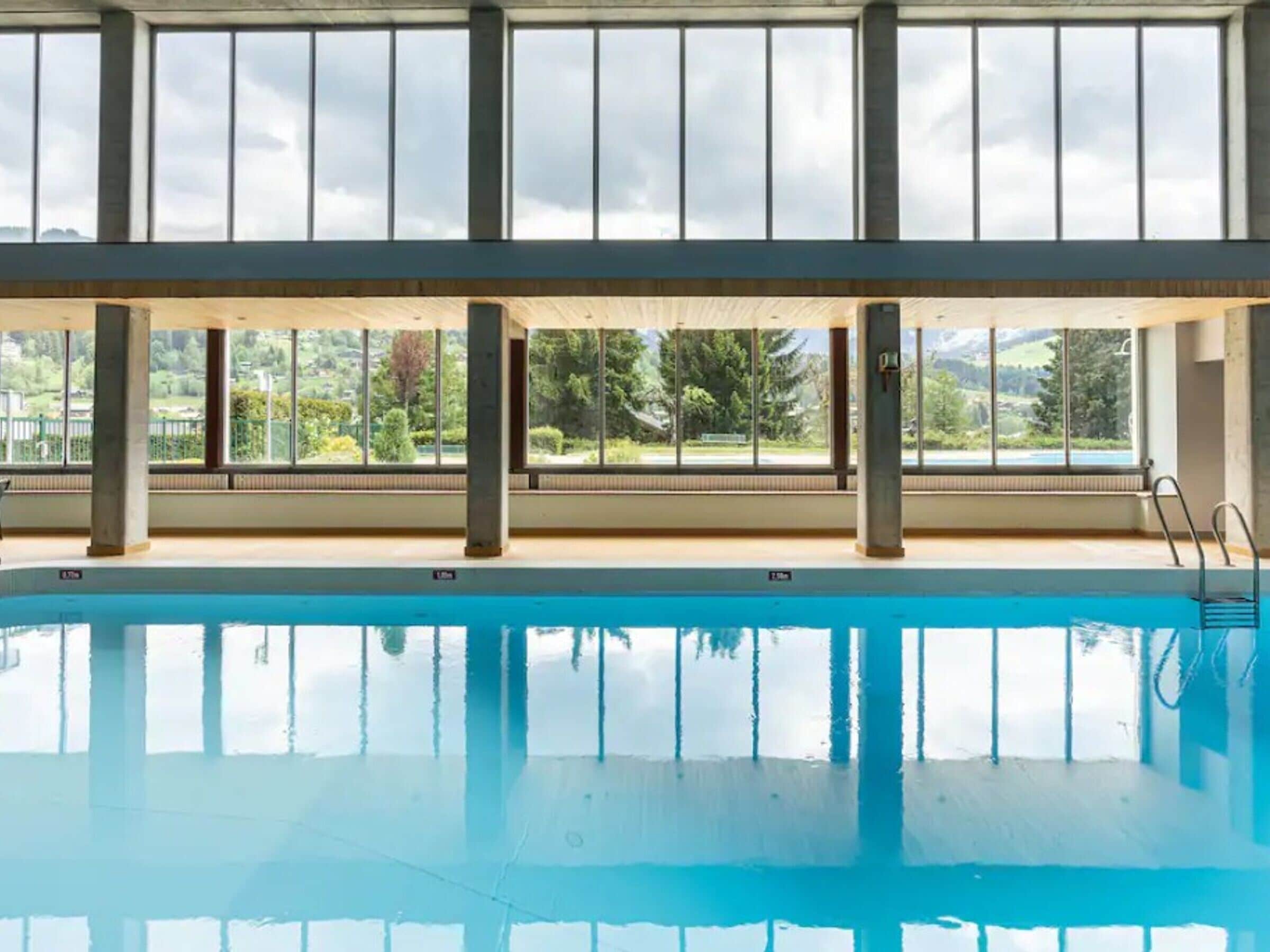An indoor swimming pool with clear views of the outdoors through large windows.