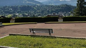 A park with a bench, a paved area, and a view of a town and mountains in the distance. - Charming lodging in Megève - 6 guests (Megève)