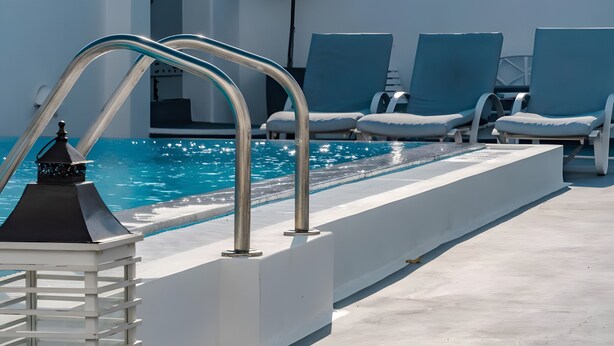 A poolside area with a metal pool ladder, lounge chairs, and a clear view of the pool. - Apartment 'One Bedroom House 25sqm' with Wi-Fi and Air Conditioning (Fira)