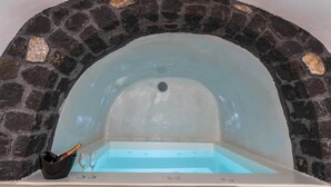 A stone-walled hot tub with a clear blue interior, a small black bucket, and two empty glasses. - Apartment 'One Bedroom House 25sqm' with Wi-Fi and Air Conditioning (Fira)