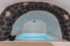 Ein Whirlpool mit Steinwänden, blauem Wasser, einem kleinen schwarzen Eimer und zwei leeren Gläsern.