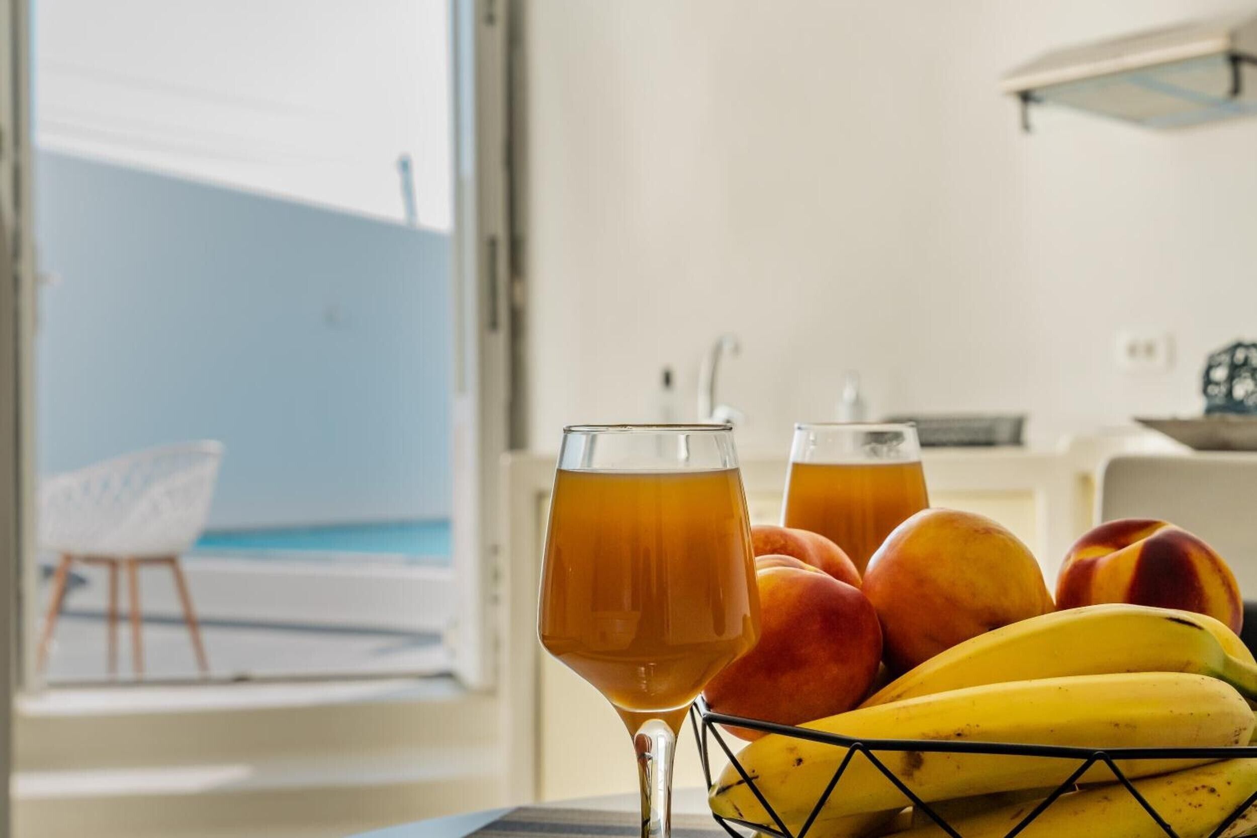 Ein Essbereich mit Tisch für zwei Personen, bestehend aus einem Glas bernsteinfarbenen Getränks und einer Obstschale mit Bananen und Pfirsichen.