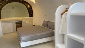 A bedroom with a bed, a built-in bench, a white wardrobe, and a stone arch above a bathtub. - Apartment 'One Bedroom House 25sqm' with Wi-Fi and Air Conditioning (Fira)