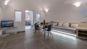 Ein moderner Wohnraum mit Essbereich, einem Flachbildfernseher und einer Couch mit gemusterten Kissen.