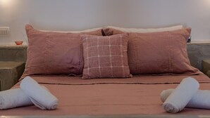 Ein Bett mit einer rosafarbenen Tagesdecke und zwei Kissen, eines gemustert und das andere schlicht.