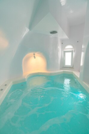A modern indoor swimming pool with a clear blue water, a sloped ceiling, and a skylight. - Apartment 'Holiday Home 28sqm' with Wi-Fi and Air Conditioning (Fira)