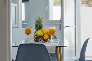 A table with a fruit bowl containing pineapple, mangoes, and bananas, and two glasses of orange juice. - Apartment 'Holiday Home 28sqm' with Wi-Fi and Air Conditioning (Fira)