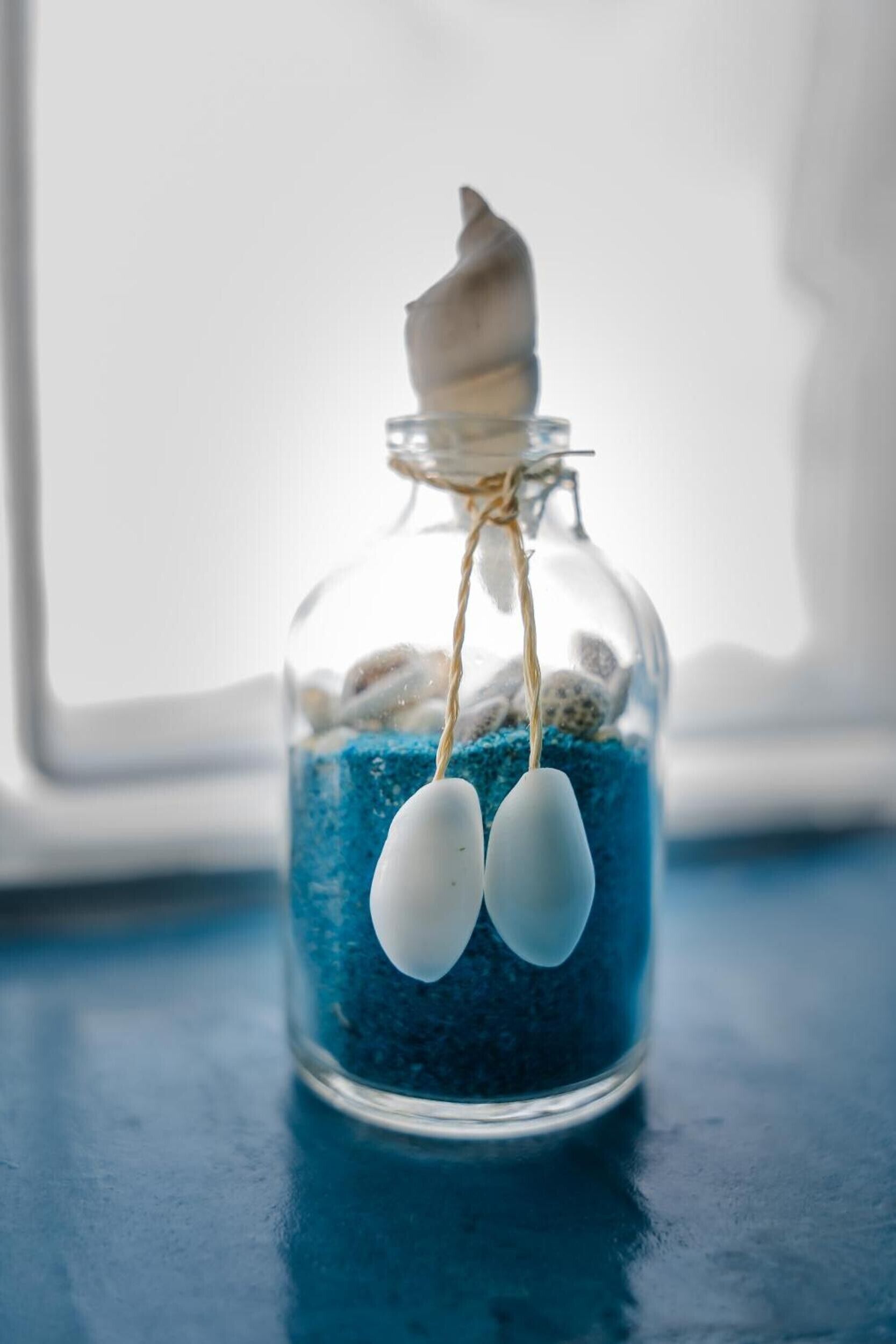 A glass jar with a white object inside, containing blue pebbles and two white objects hanging from a string.