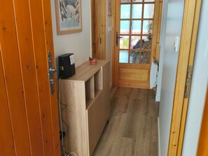Un pasillo estrecho con suelo de madera, una puerta con paneles de vidrio esmerilado y un pequeño banco de madera con una cesta encima.