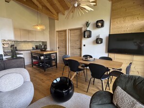 A modern living space with a dining area, kitchen, and a flat-screen TV mounted on the wall. - Apartment with private parking - 6 guests (Les Carroz d'Arâches)