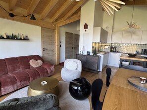 A modern living room with a red sofa, a grey armchair, and a wooden dining table. - Apartment with private parking - 6 guests (Les Carroz d'Arâches)