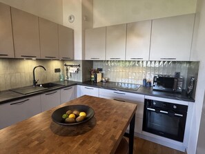 A modern kitchen with a wooden table, a bowl of fruit, and a built-in oven. - Apartment with private parking - 6 guests (Les Carroz d'Arâches)