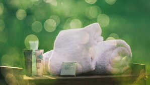 A white towel, a bottle, and a box on a wooden surface with a green bokeh background.