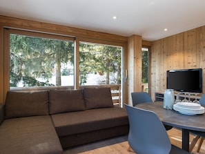 A modern living room with a sofa, dining table, chairs, and a TV.