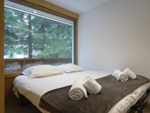 Ein Schlafzimmer mit großem Fenster, zwei Betten und ordentlich gefalteten Handtüchern.