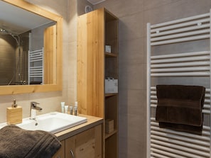 Ein Badezimmer mit einem Holzbadezimmerhocker, einem weißen Waschbecken, einem Spiegel und einem Handtuchhalter.