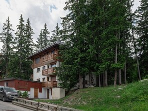 A multi-story building with balconies, surrounded by dense forest.