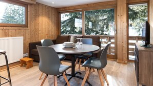 A modern room with a round table, chairs, a sofa, and large windows with a view of trees.