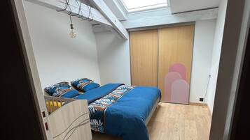 Une chambre avec un puits de lumière, un lit recouvert d’une couverture bleue et une armoire.