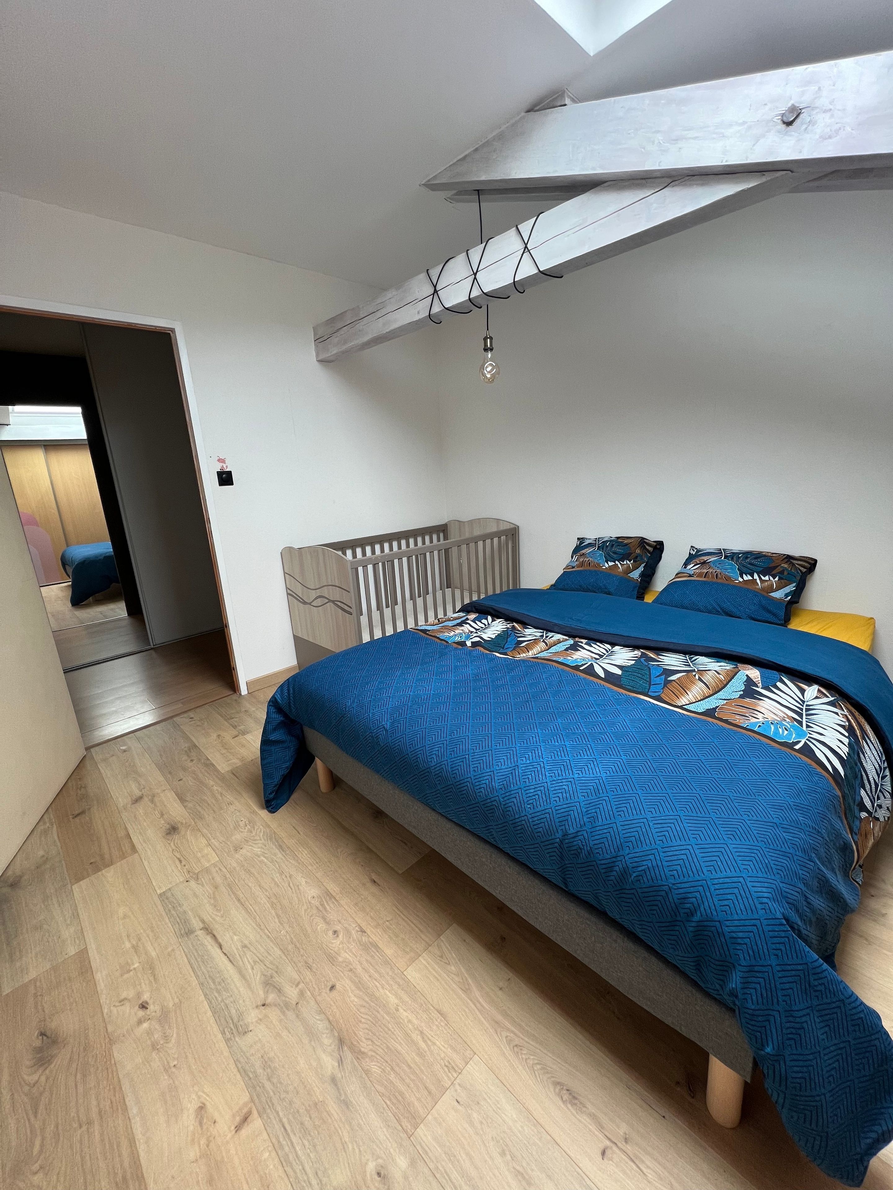 Een slaapkamer met een bed, een houten vloer, een plafond met een lamp en een deur naar een andere kamer.