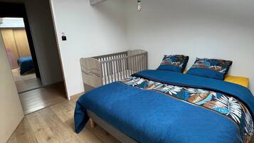 Een slaapkamer met een bed, een houten vloer, een plafond met een lamp en een deur naar een andere kamer.
