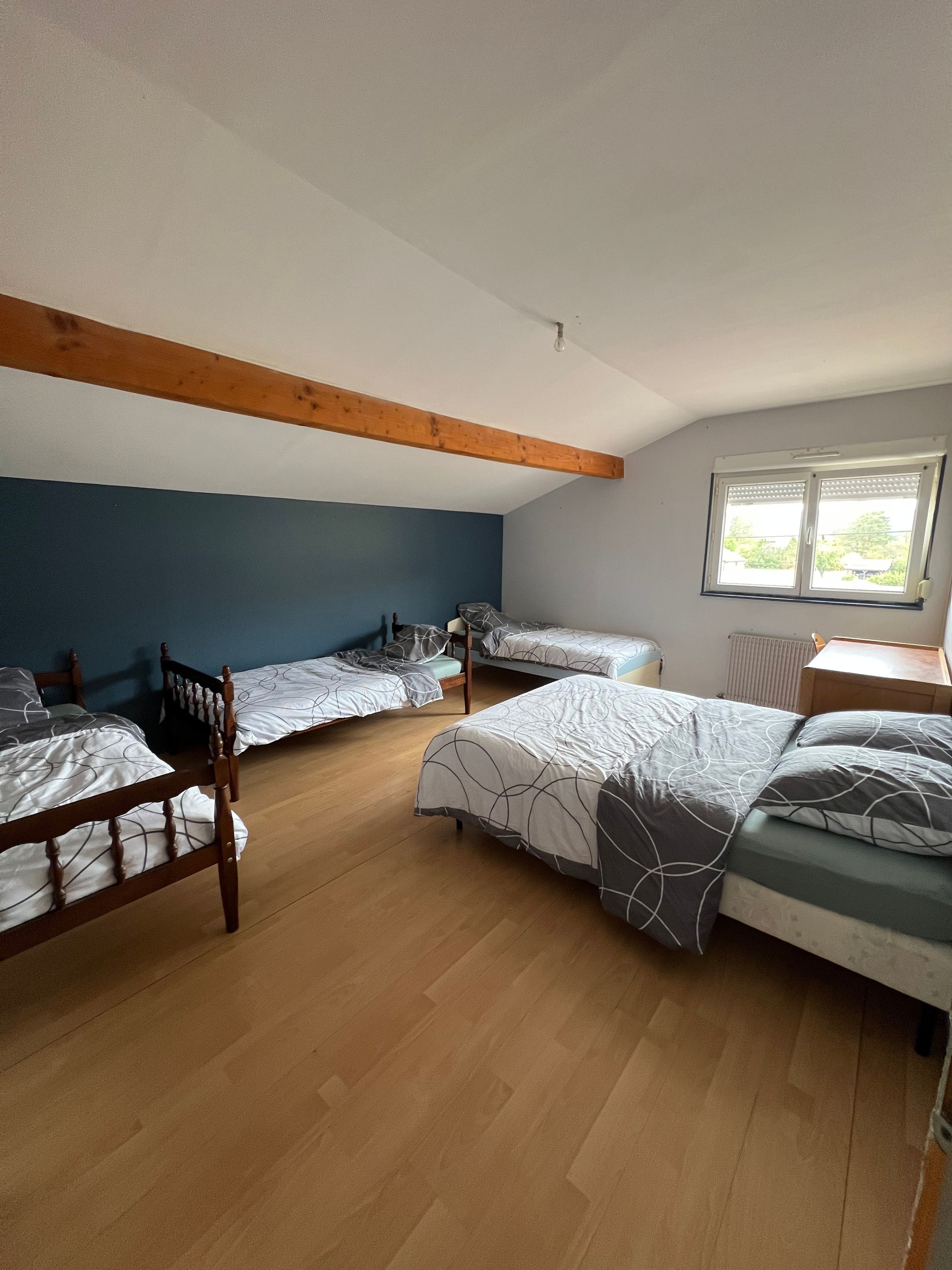 Una camera del dormitorio con quattro letti singoli, travi in legno a soffitto, una finestra con persiane e un termosifone.